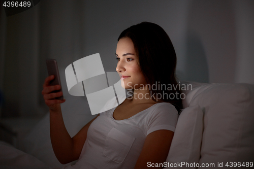 Image of happy young woman with smartphone in bed at night