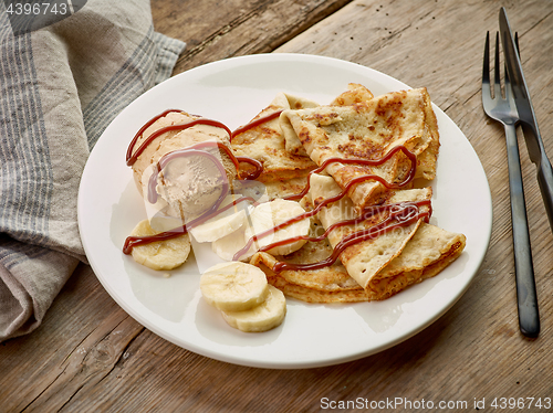 Image of Crepes with banana and caramel icecream on wooden desk