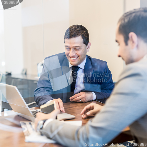 Image of Two young businessmen using laptop computer at business meeting.