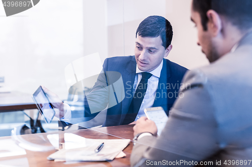 Image of Two young businessmen using electronic devices at business meeting.