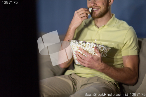 Image of close up of man with popcorn watching tv at night