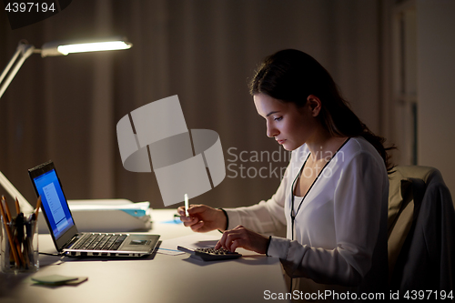 Image of woman with calculator and papers at night office