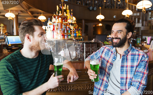 Image of male friends drinking green beer at bar or pub