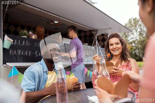 Image of happy friends with drinks eating at food truck