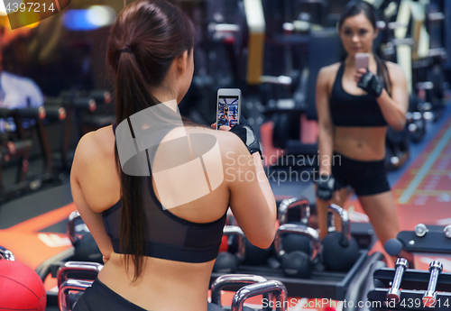 Image of woman with smartphone taking mirror selfie in gym