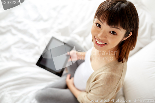 Image of happy pregnant asian woman with tablet pc at home