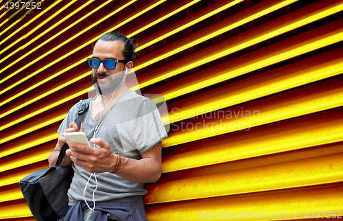 Image of man with earphones and smartphone over wall