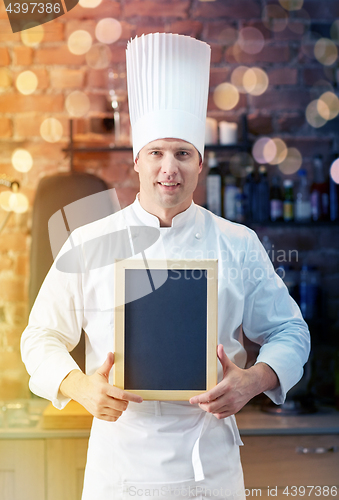 Image of happy male chef with blank menu board in kitchen