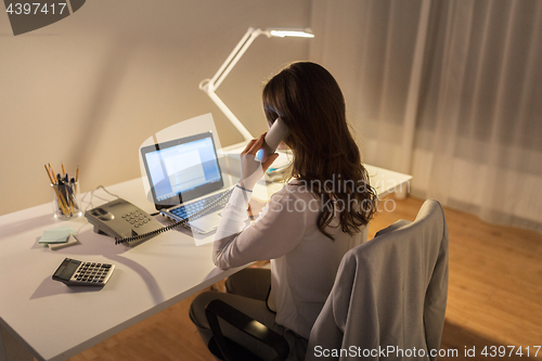 Image of woman with laptop calling on phone at night office