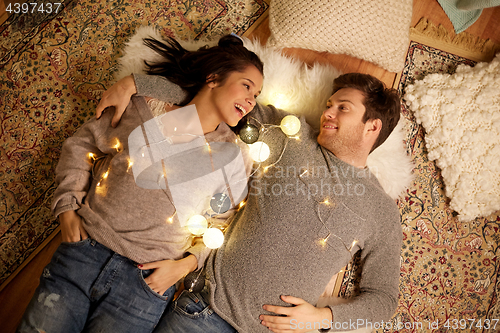 Image of happy couple with garland lying on floor at home