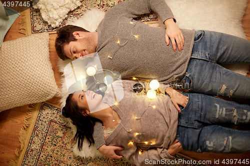 Image of happy couple with garland lying on floor at home