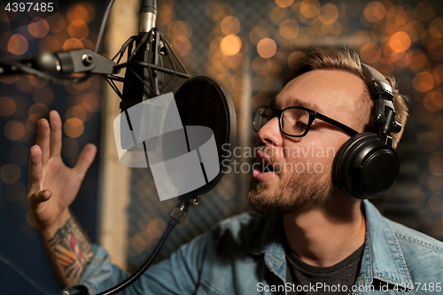 Image of man with headphones singing at recording studio