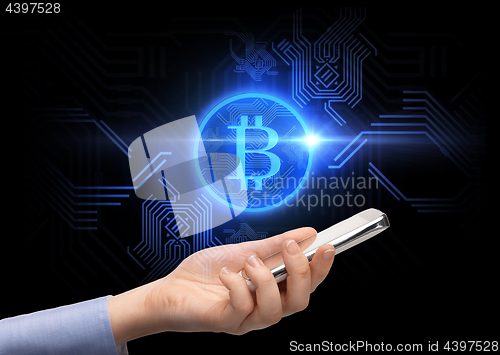 Image of close up of hand with smartphone and bitcoin