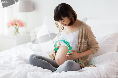 Image of happy pregnant woman with headphones at home