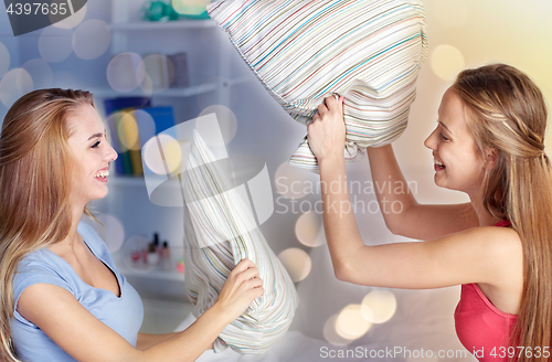 Image of happy teen girl friends fighting pillows at home