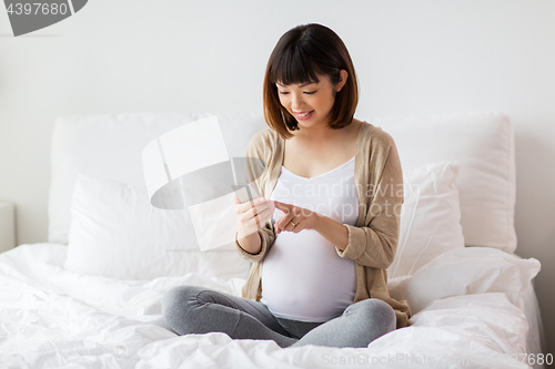 Image of pregnant woman with smartphone in bed at home