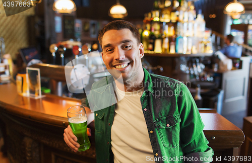 Image of man drinking green beer at bar or pub
