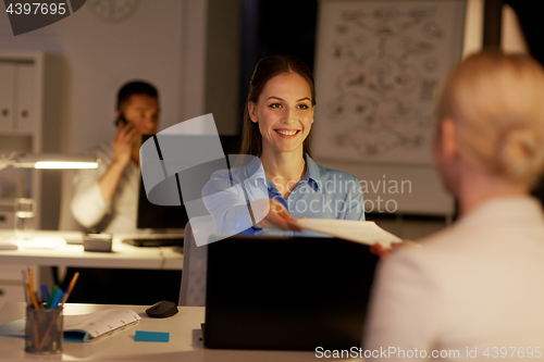 Image of businesswomen with papers working late at office