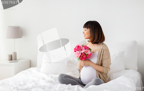 Image of happy asian pregnant woman with flowers in bed