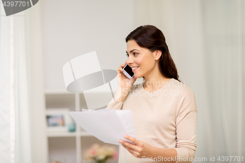 Image of woman with papers calling on smartphone at home