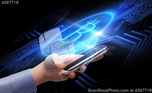 Image of close up of hand with smartphone and bitcoin