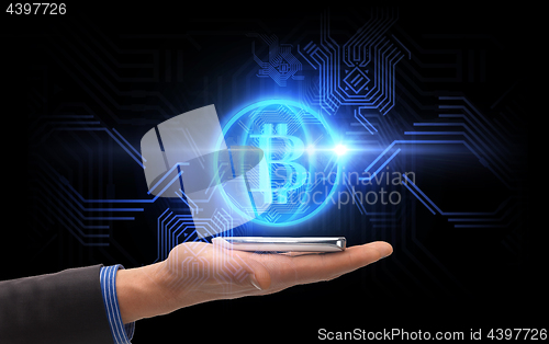 Image of close up of hand with smartphone and bitcoin