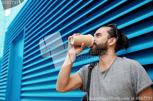 Image of man drinking coffee from paper cup over wall