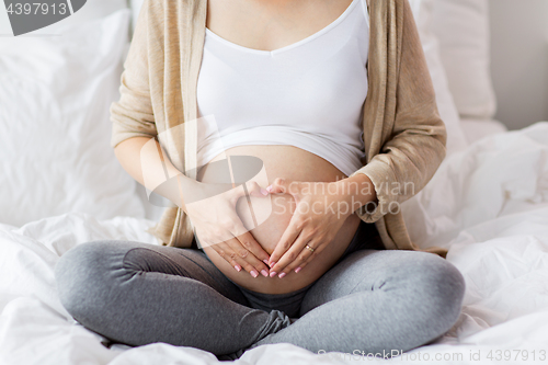 Image of happy pregnant woman making heart gesture in bed