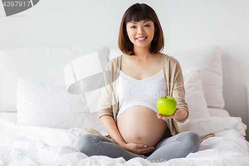 Image of happy pregnant woman with apple in bed at home