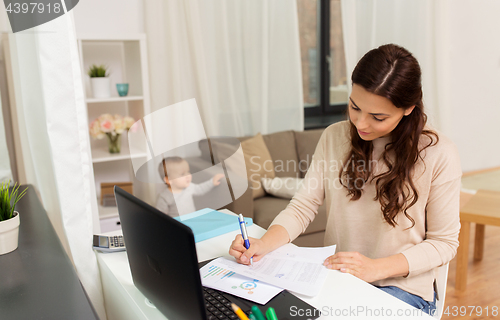 Image of happy mother with baby and papers working at home