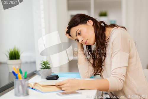 Image of tired female student with book learning at home