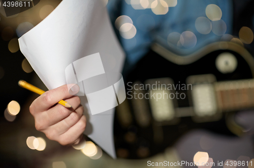 Image of man with guitar, pencil and paper at music studio