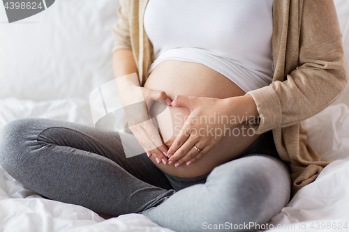 Image of happy pregnant woman making heart gesture in bed