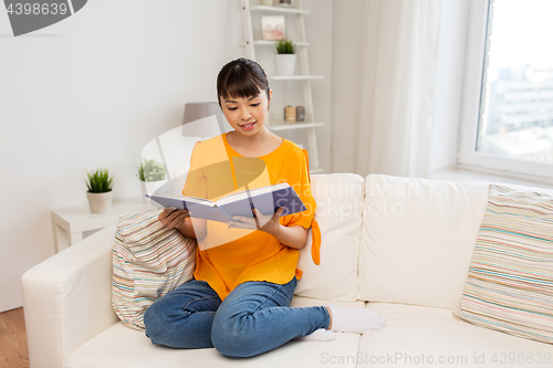 Image of smiling young asian woman reading book at home