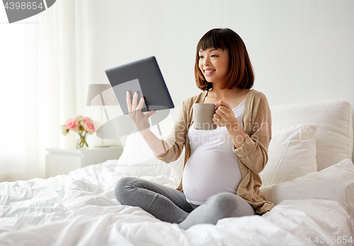 Image of happy pregnant asian woman with tablet pc at home