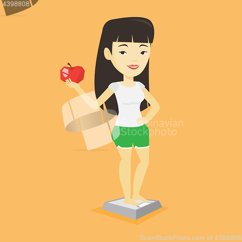 Image of Woman standing on scale and holding apple in hand.