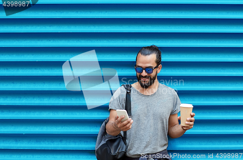 Image of man with coffee cup and smartphone over blue wall