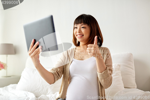 Image of happy pregnant asian woman with tablet pc at home