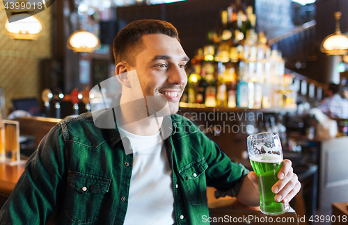 Image of man drinking green beer at bar or pub