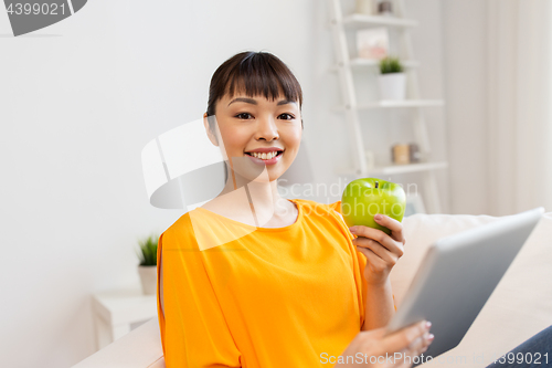 Image of happy asian woman with tablet pc and apple at home