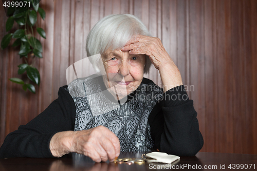 Image of Elderly woman sitting at the table counting money in her wallet.