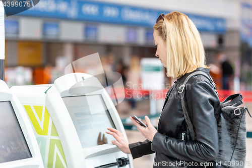 Image of Casual caucasian woman using smart phone application and check-in machine at the airport getting the boarding pass.