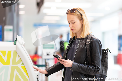 Image of Casual caucasian woman using smart phone application and check-in machine at the airport getting the boarding pass.