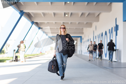 Image of Portrait of young cheerful female traveler wearing casual clothes carrying heavy backpack and luggage at airport.