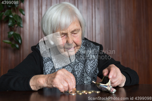 Image of Elderly woman sitting at the table counting money in her wallet.