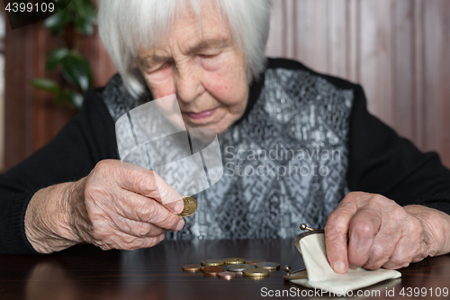 Image of Elderly woman sitting at the table counting money in her wallet.