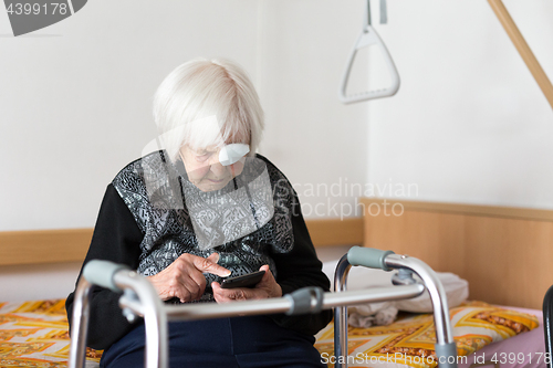 Image of Lonley elderly 95 years old woman sitting at the bad using modern mobile phone.