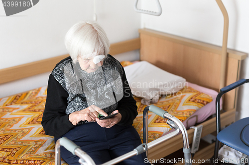 Image of Lonley elderly 95 years old woman sitting at the bad using modern mobile phone.