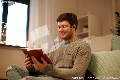 Image of happy young man reading book at home