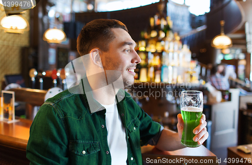 Image of man drinking green beer at bar or pub